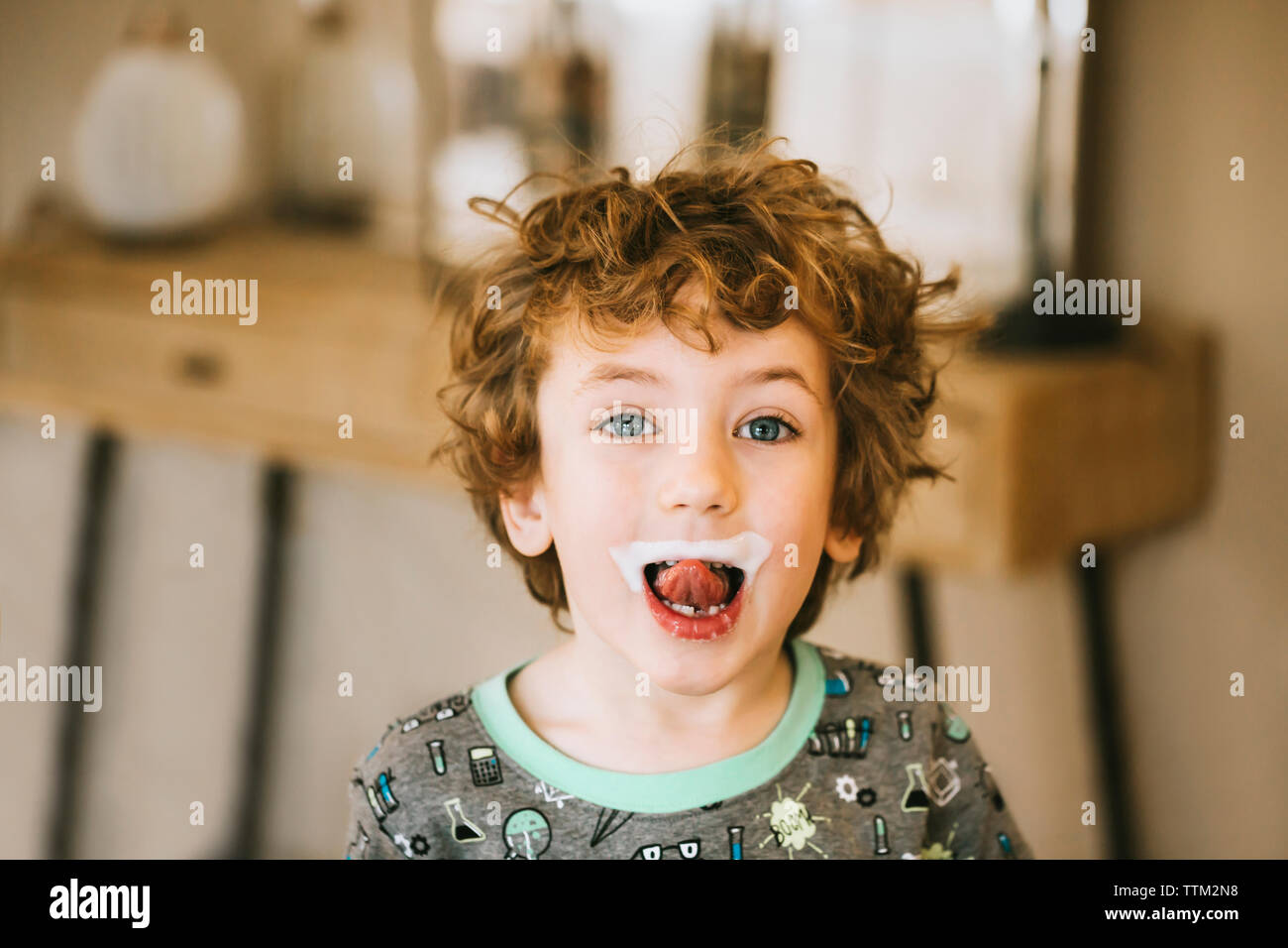 Portrait of cute boy with milk mustache sticking out tongue at home Stock Photo