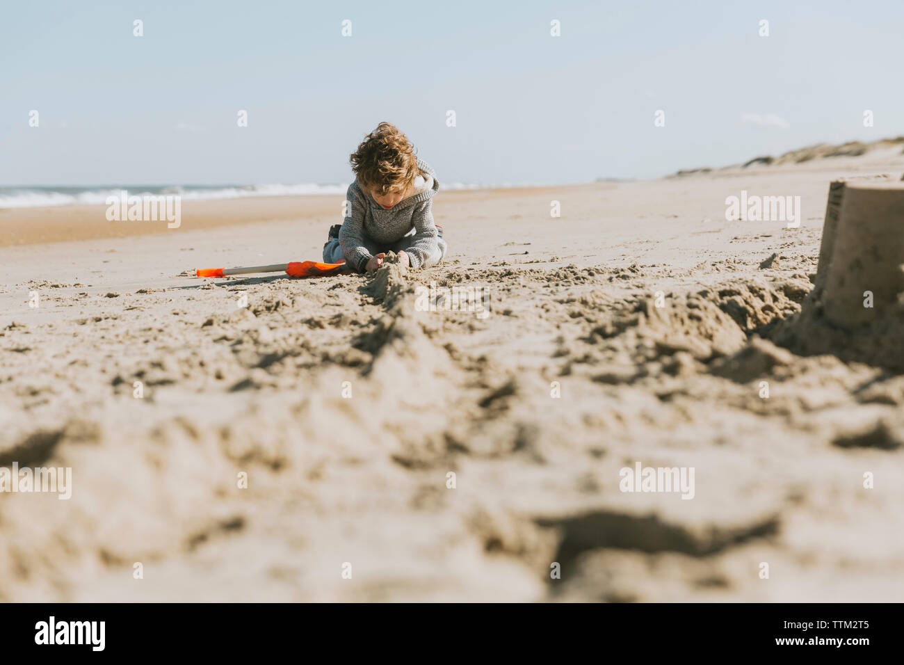 Boy making sandcastle at beach against clear sky during sunny day Stock Photo