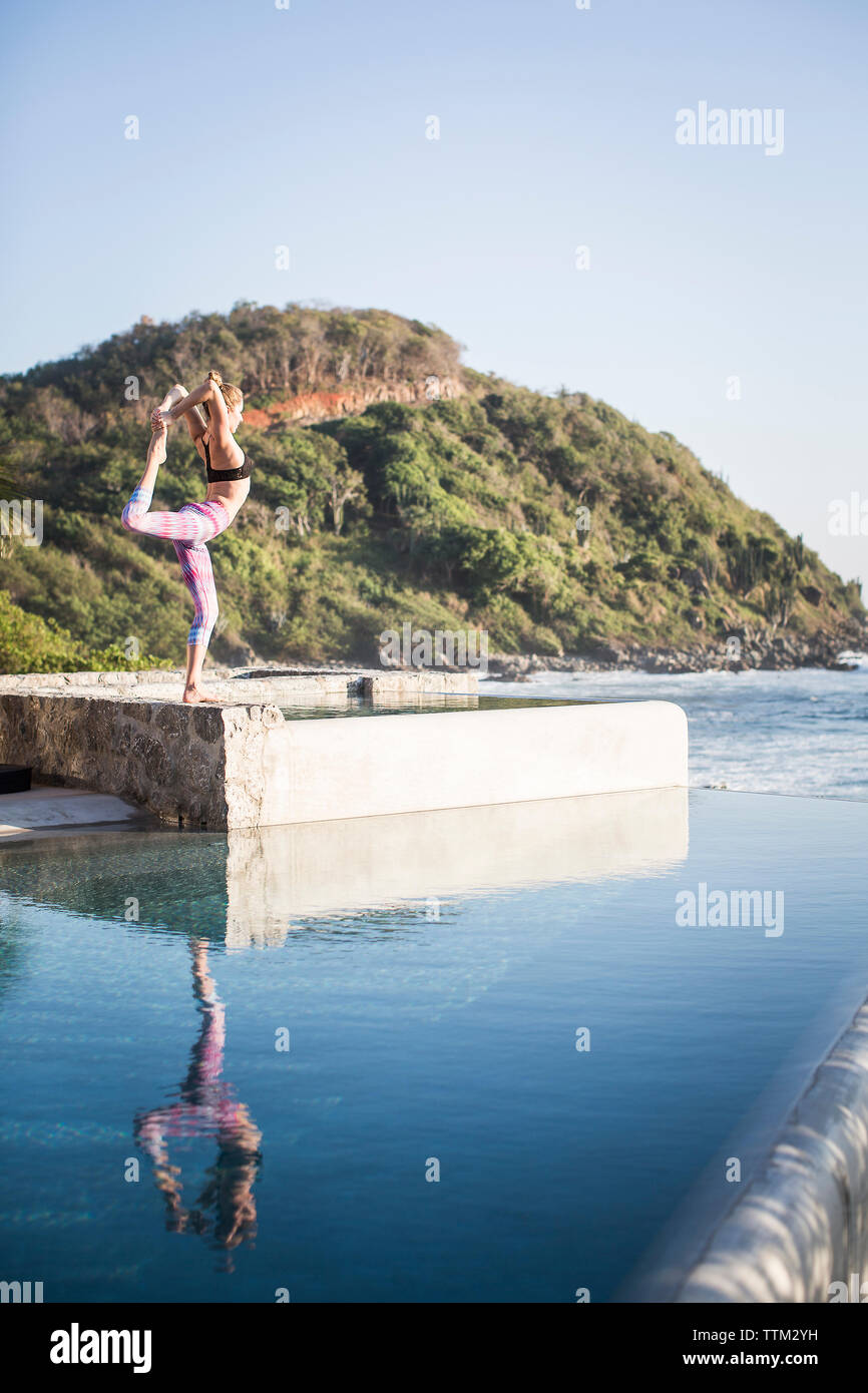 Side view of woman exercising on poolside against clear sky Stock Photo