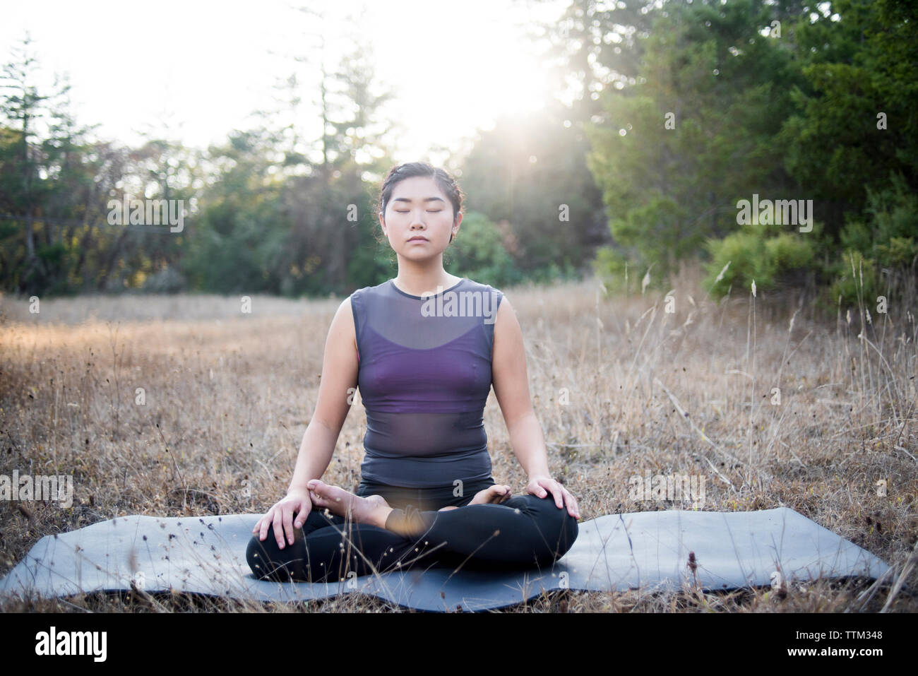 Woman meditating while sitting on exercise mat at field Stock Photo
