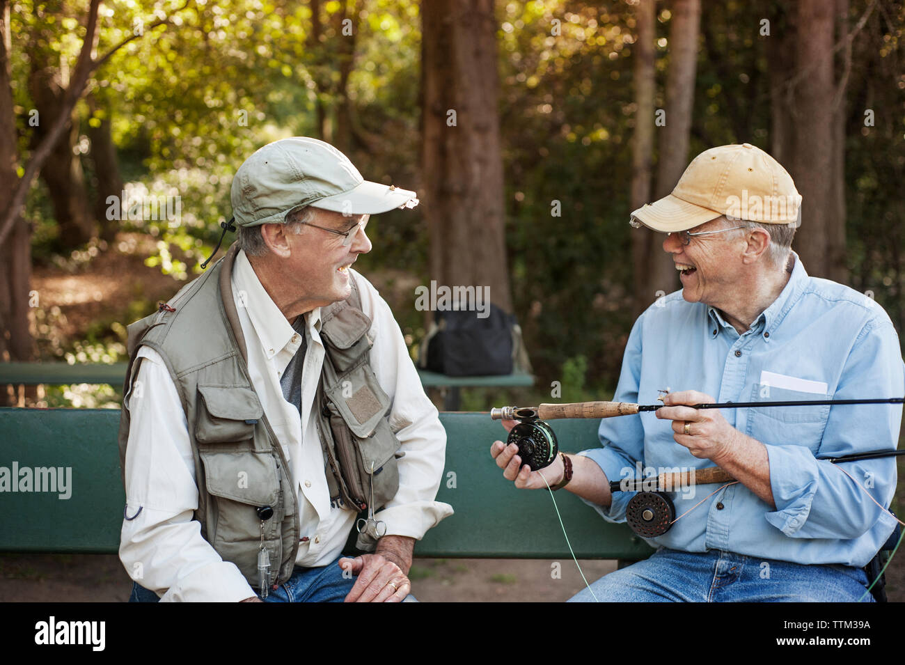 Cheerful senior man talking to friend while holding fishing rods in forest Stock Photo