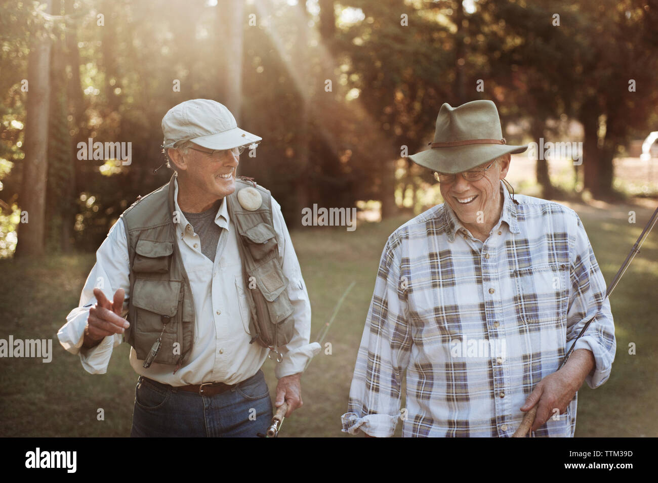 Happy senior men holding fishing rods while walking in forest Stock Photo