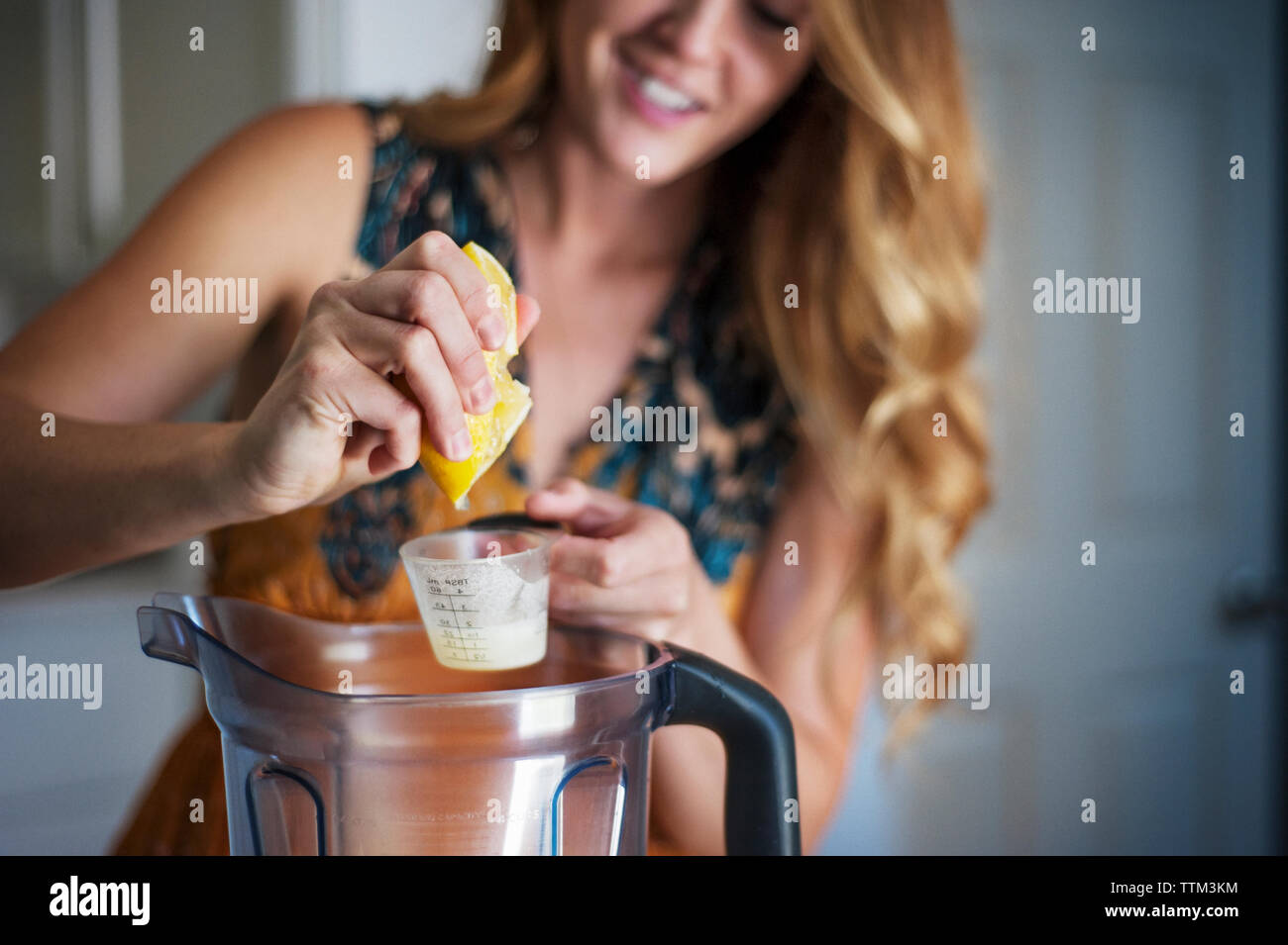 Woman squeezing lemon in cup over jar Stock Photo