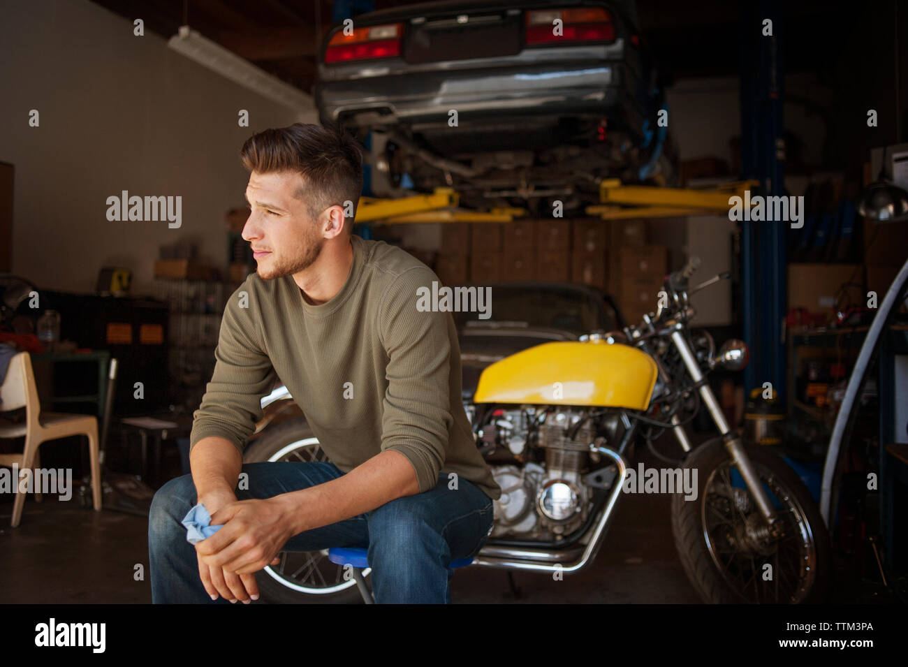 Man looking away while sitting on stool in garage Stock Photo