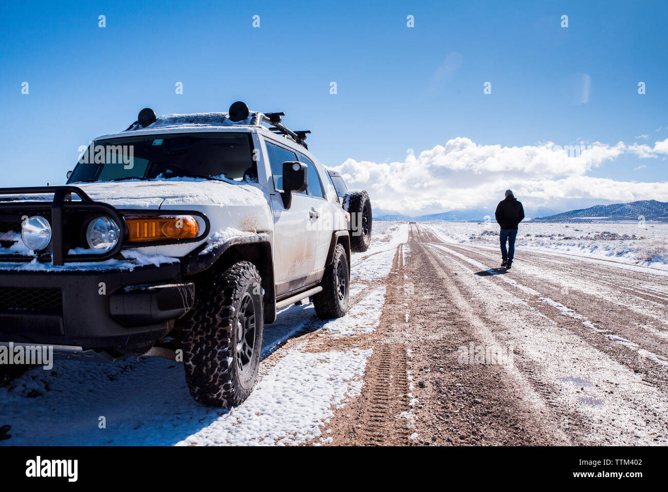 Rear view of man with off-road vehicle on dirt road amidst desert during winter Stock Photo
