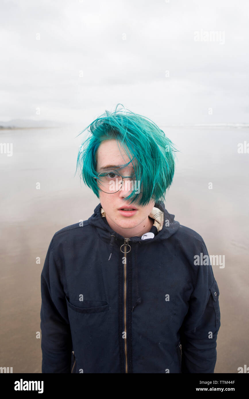 Portrait of teenage girl with green hair standing at beach against cloudy sky Stock Photo