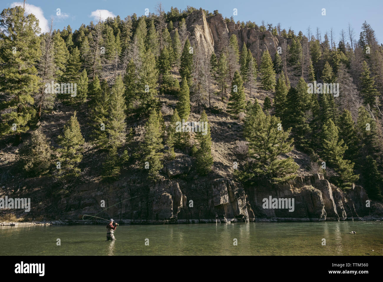 Side view of man fishing in river by mountain at forest Stock Photo