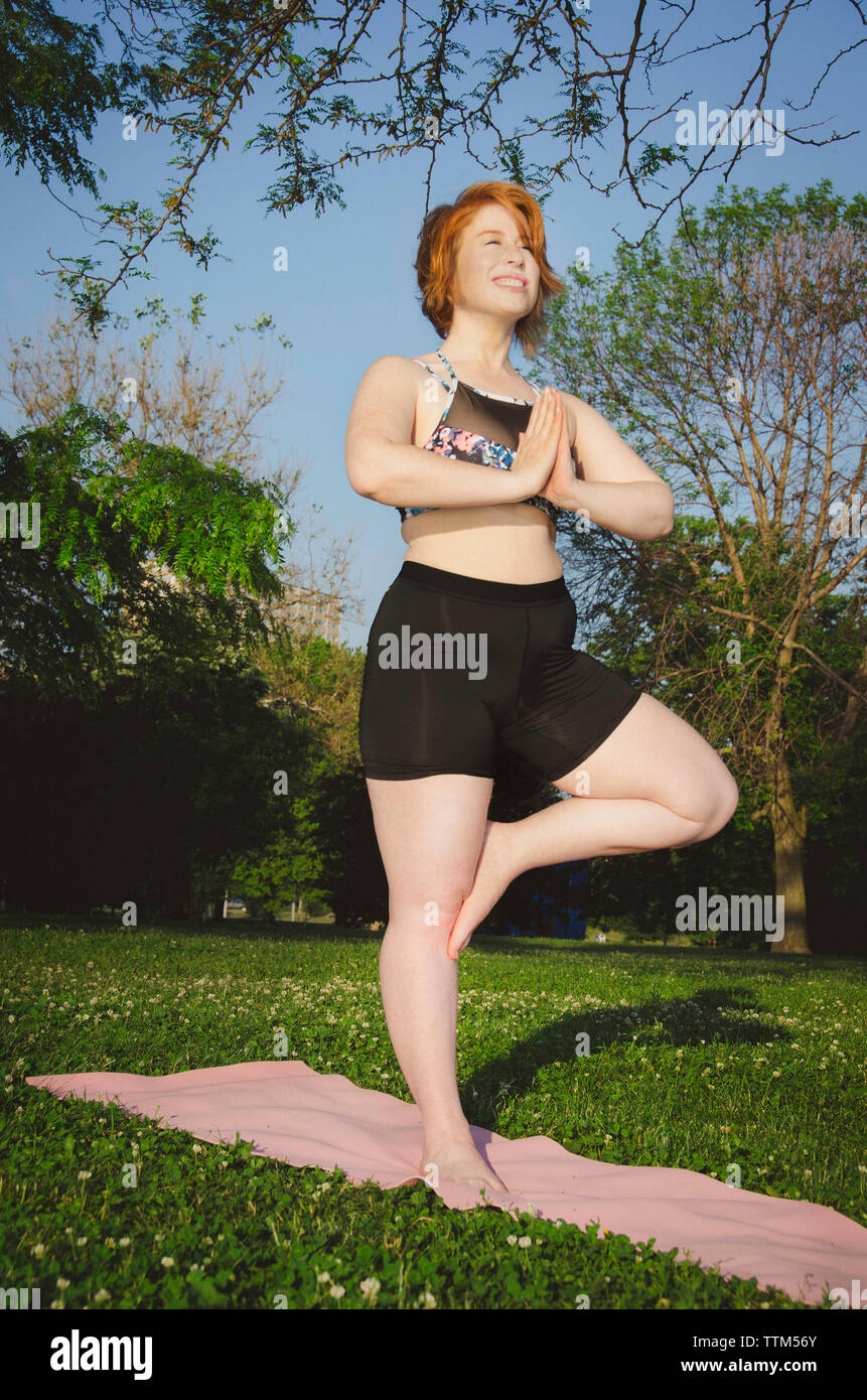 Low angle view of woman practicing tree pose yoga at park Stock Photo
