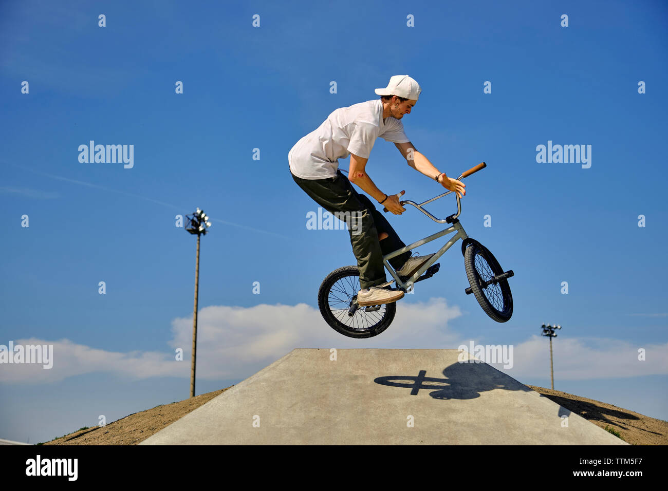 Man with BMX bike practicing barspin on sports ramp against blue sky during sunny day Stock Photo