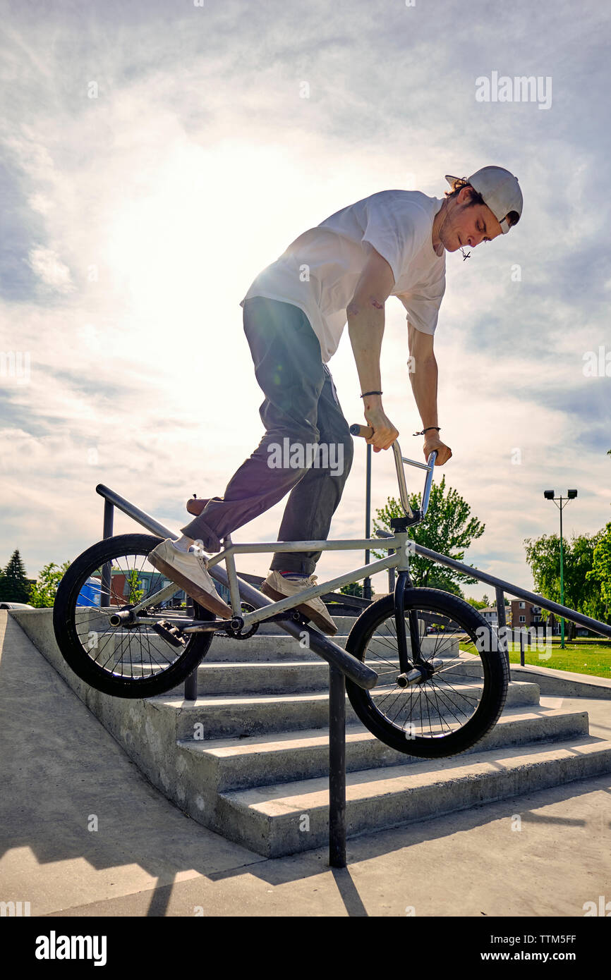 Rider riding BMX bike on railing at skateboard park against sky during sunny day Stock Photo