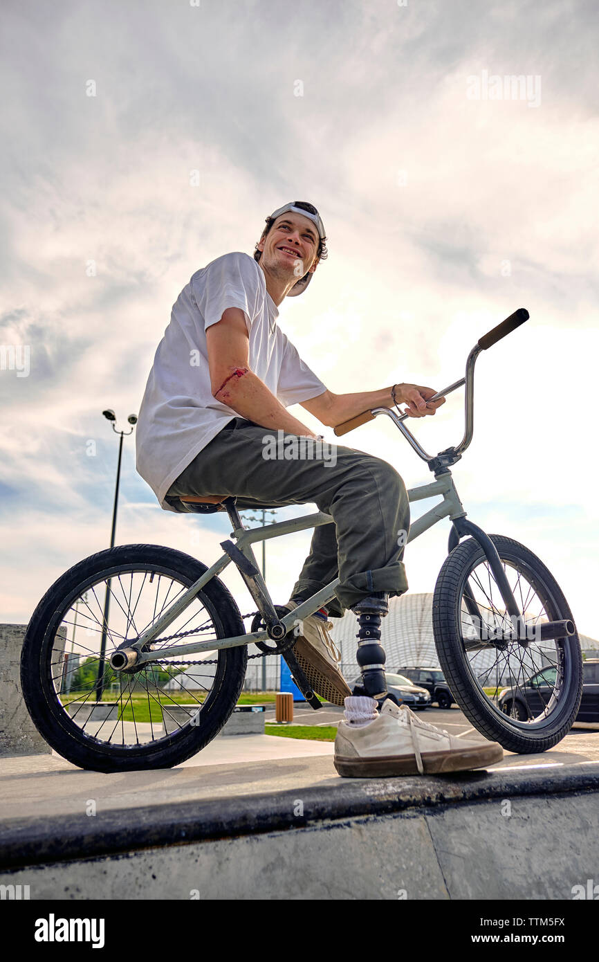BMX rider with prosthetic foot confidently posing on bike against cloudy sky at skateboard park Stock Photo