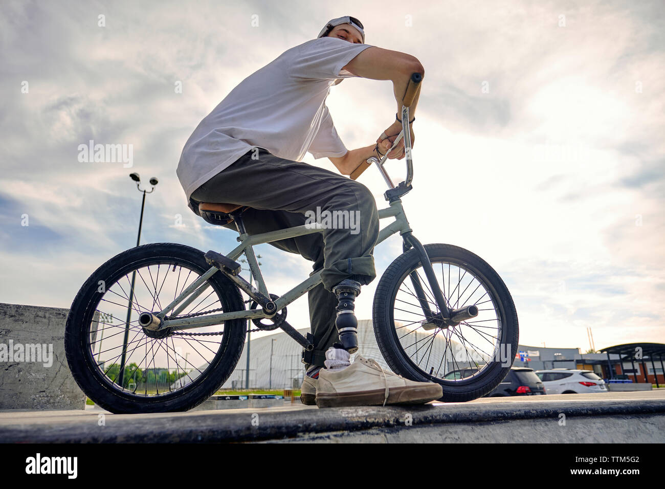 BMX rider with prosthetic foot confidently posing on bike against cloudy sky at skateboard park Stock Photo