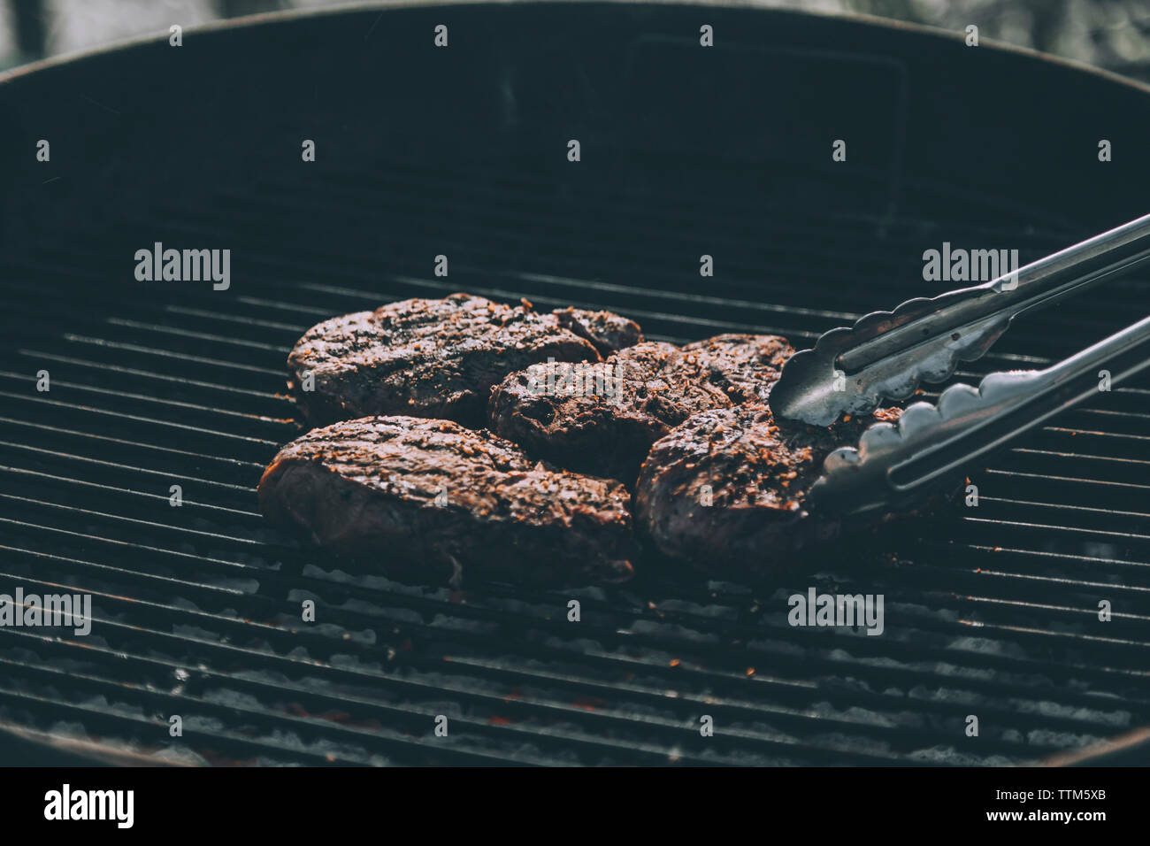 High angle view of steak and servings tongs on barbeque grill Stock