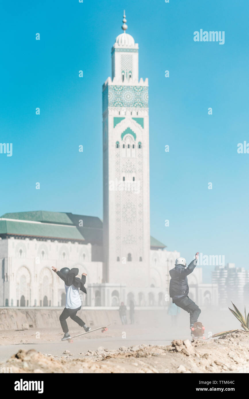 Full length of friends skateboarding against Mosque Hassan II Stock Photo