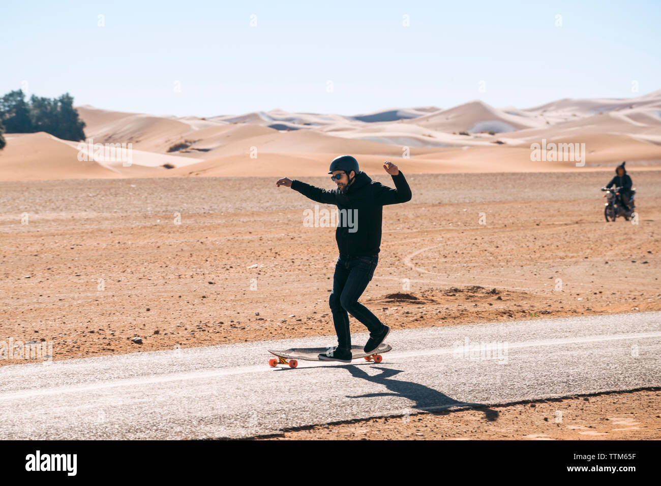 Full length of man skateboarding on road amidst field against sky during sunny day Stock Photo