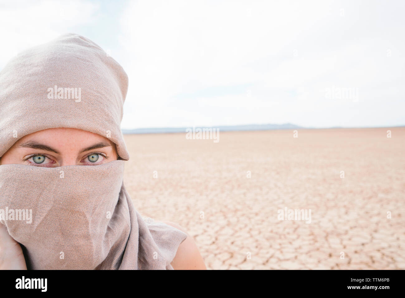 Portrait of woman wearing scarf standing at barren landscape against sky during sunny day Stock Photo