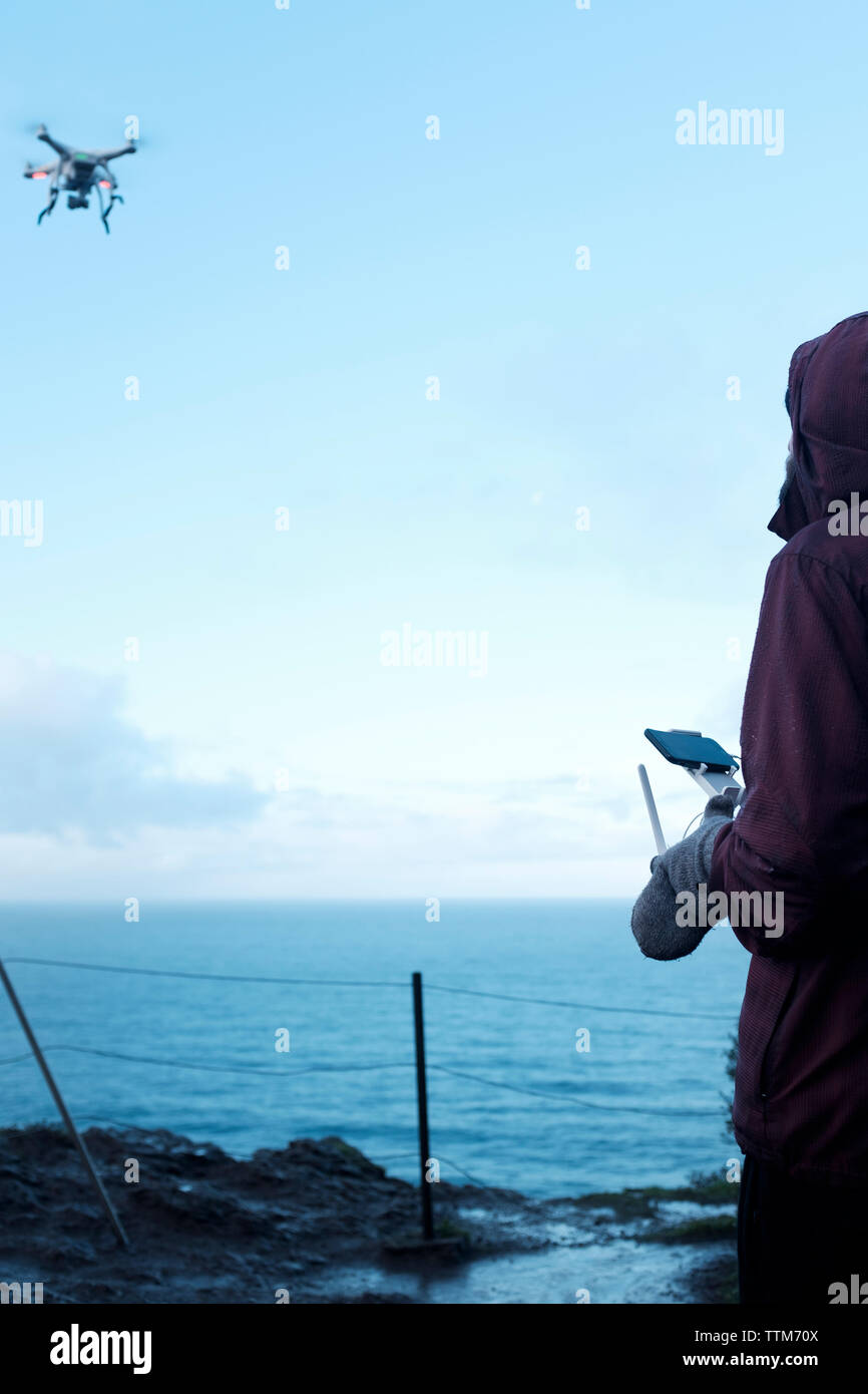 Hiker flying drone over sea against sky Stock Photo