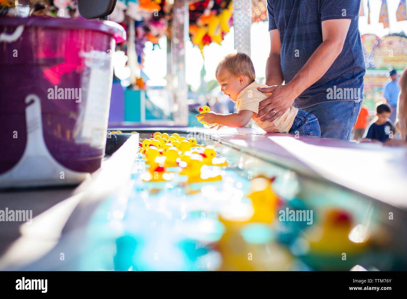 Father lifting son playing with rubber ducks floating in water at amusement park Stock Photo