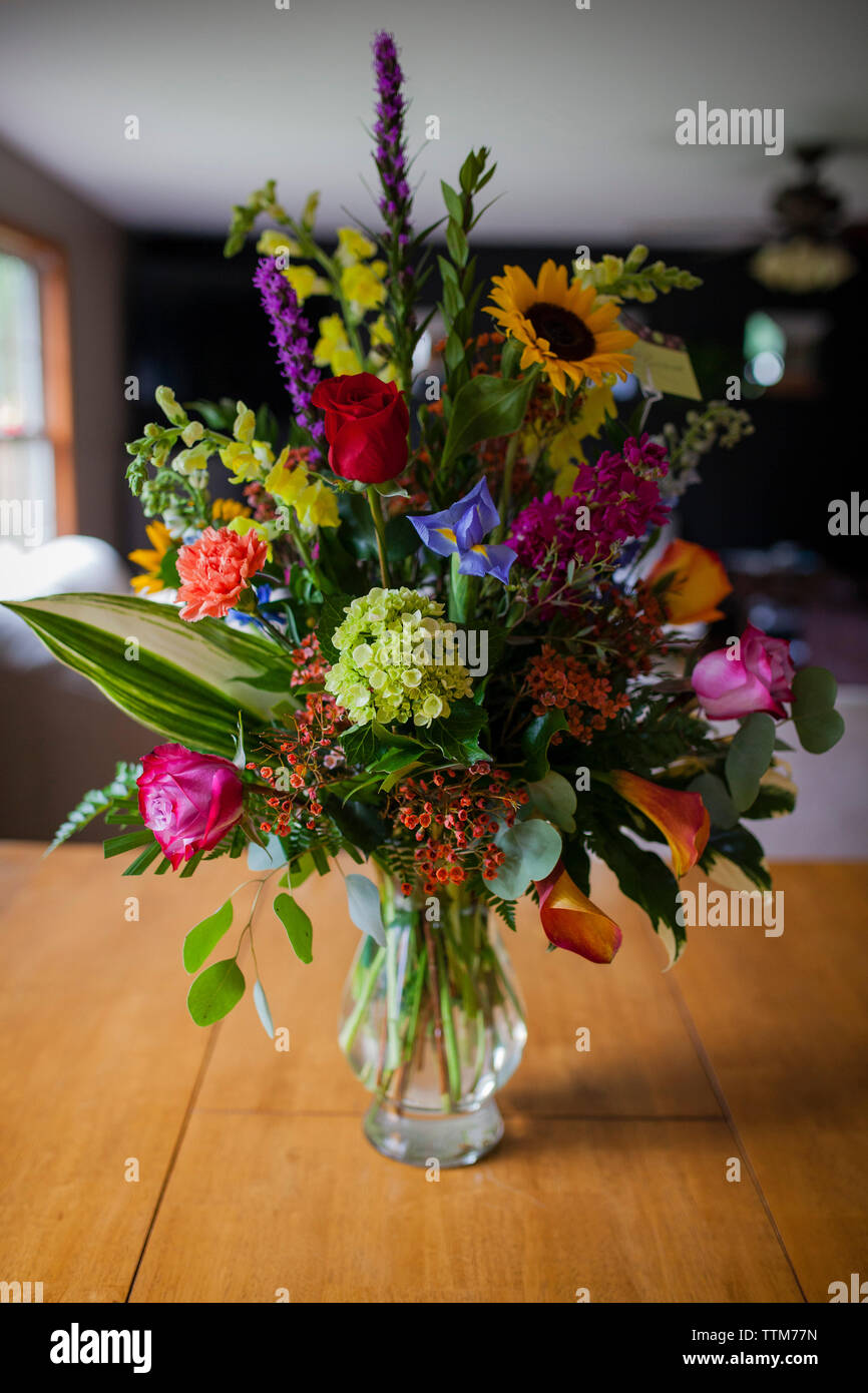 Various flowers in glass vase on wooden table at home Stock Photo