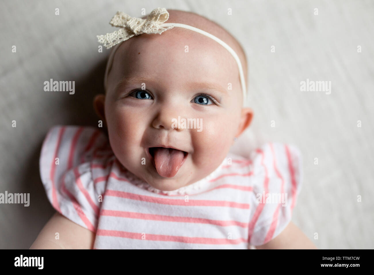 Close-up portrait of happy baby girl sticking out tongue while relaxing on bed at home Stock Photo