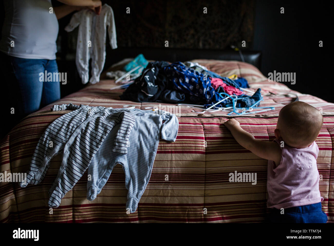 Midsection of mother holding laundry while daughter standing by bed Stock Photo