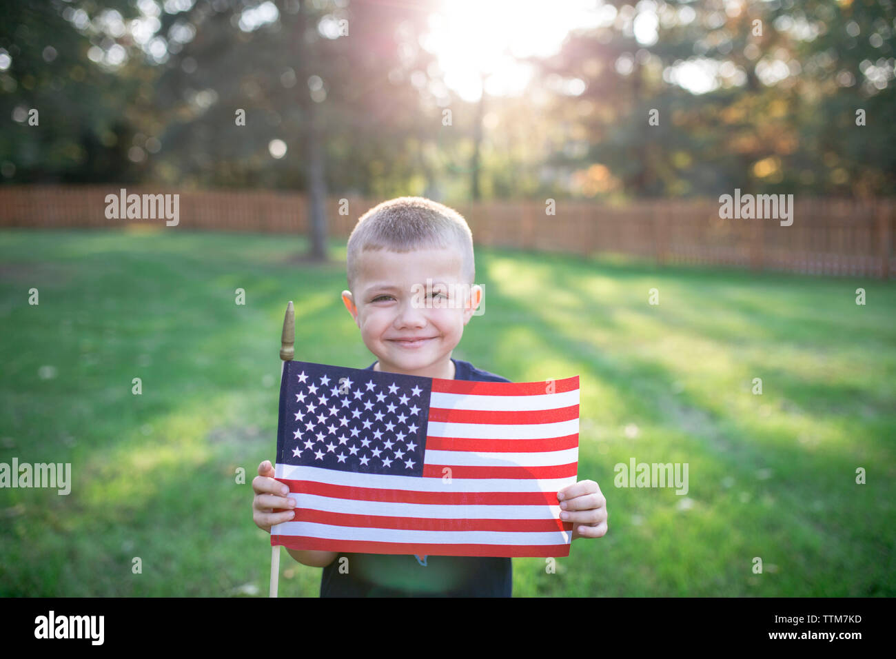 Portrait of smiling boy holding American flag while standing on field in yard Stock Photo