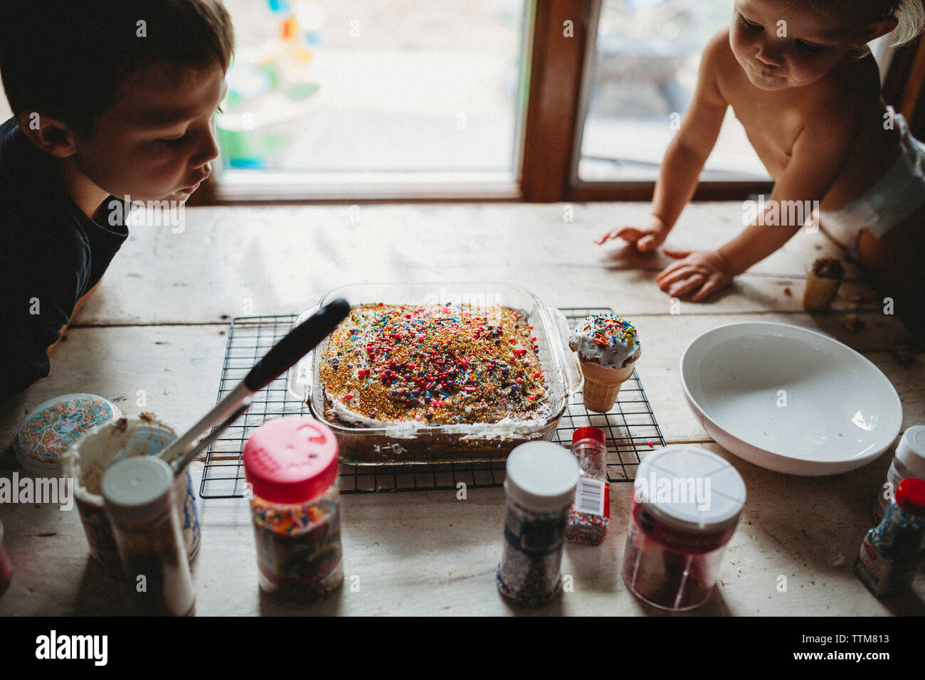 Two siblings looking at freshly baked heavily decorated sprinkled cake Stock Photo