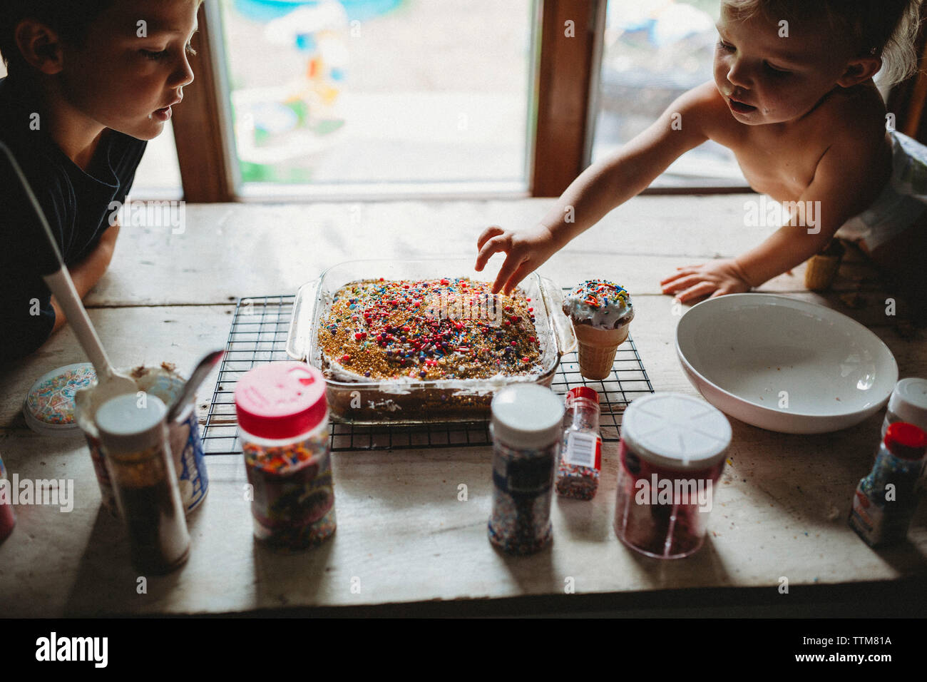 Two siblings sneaking sprinkles off of freshly baked cake treat Stock Photo