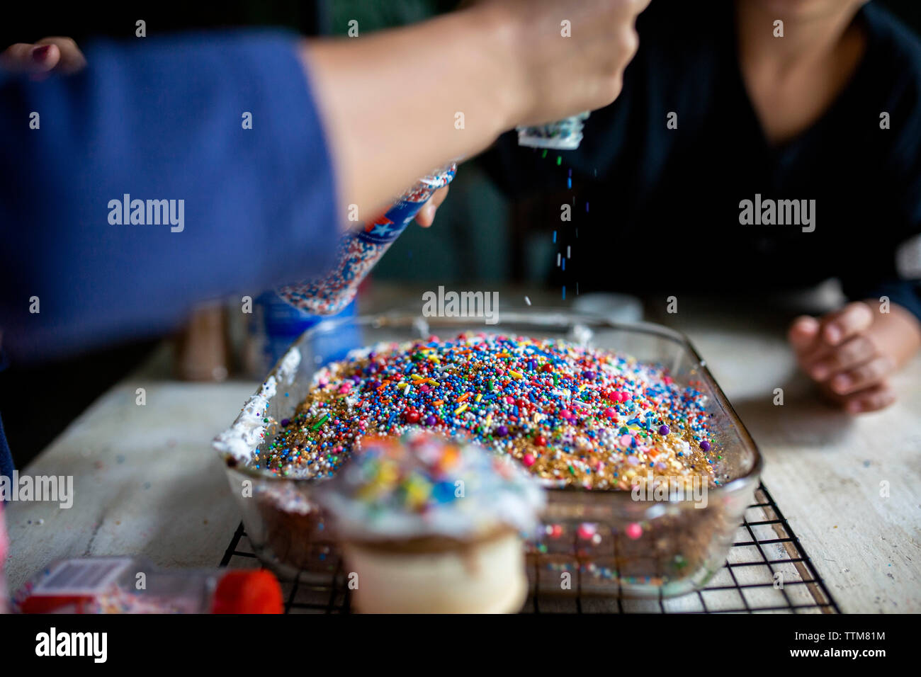 Siblings decorating cake with plenty of colorful sprinkles Stock Photo
