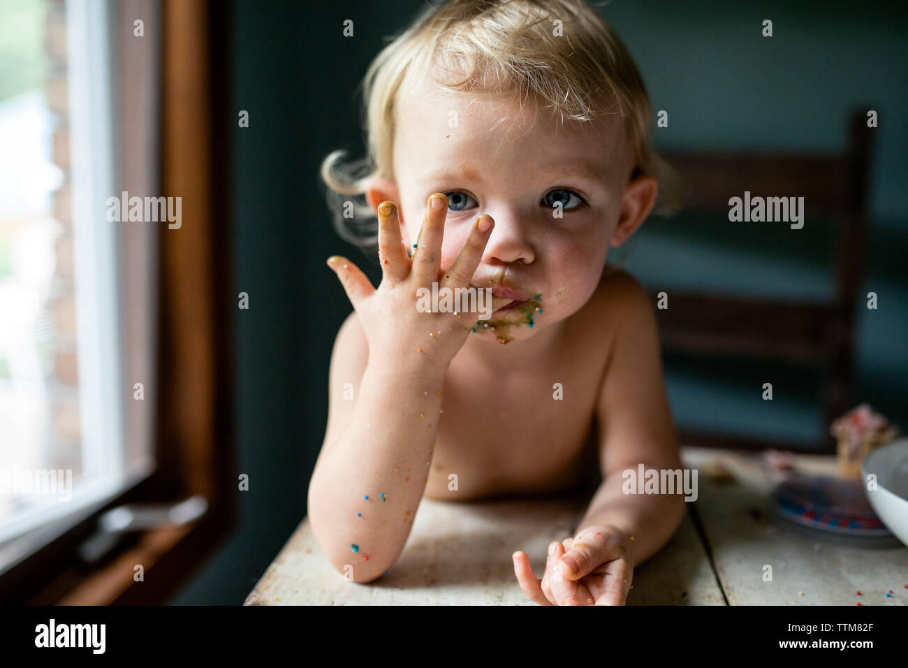 Toddler girl licking sticky fingers with colorful sprinkles Stock Photo