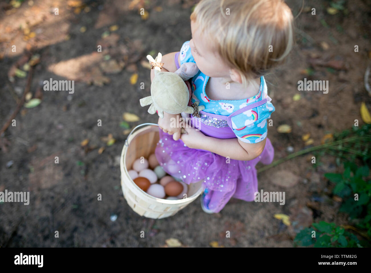 Toddler girl looking away holding baby doll and basket of eggs Stock Photo