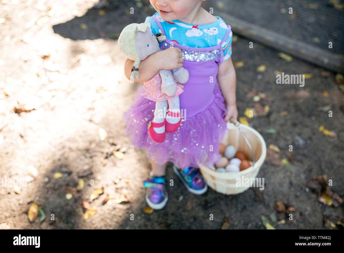 Happy toddler girl with baby doll dressed up with basket of eggs Stock Photo