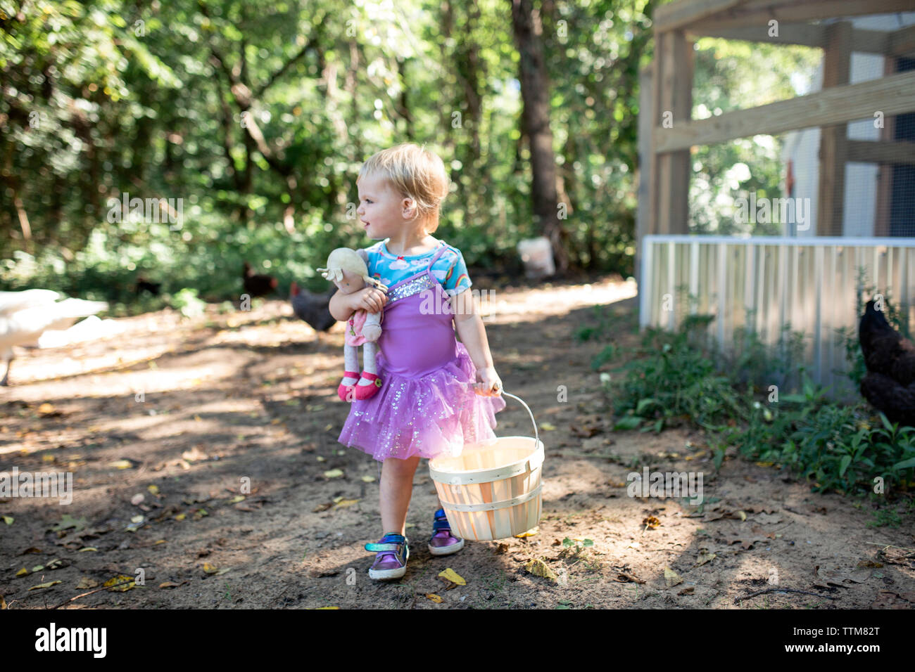 Toddler girl looking away carrying basket and baby doll dressed up Stock Photo