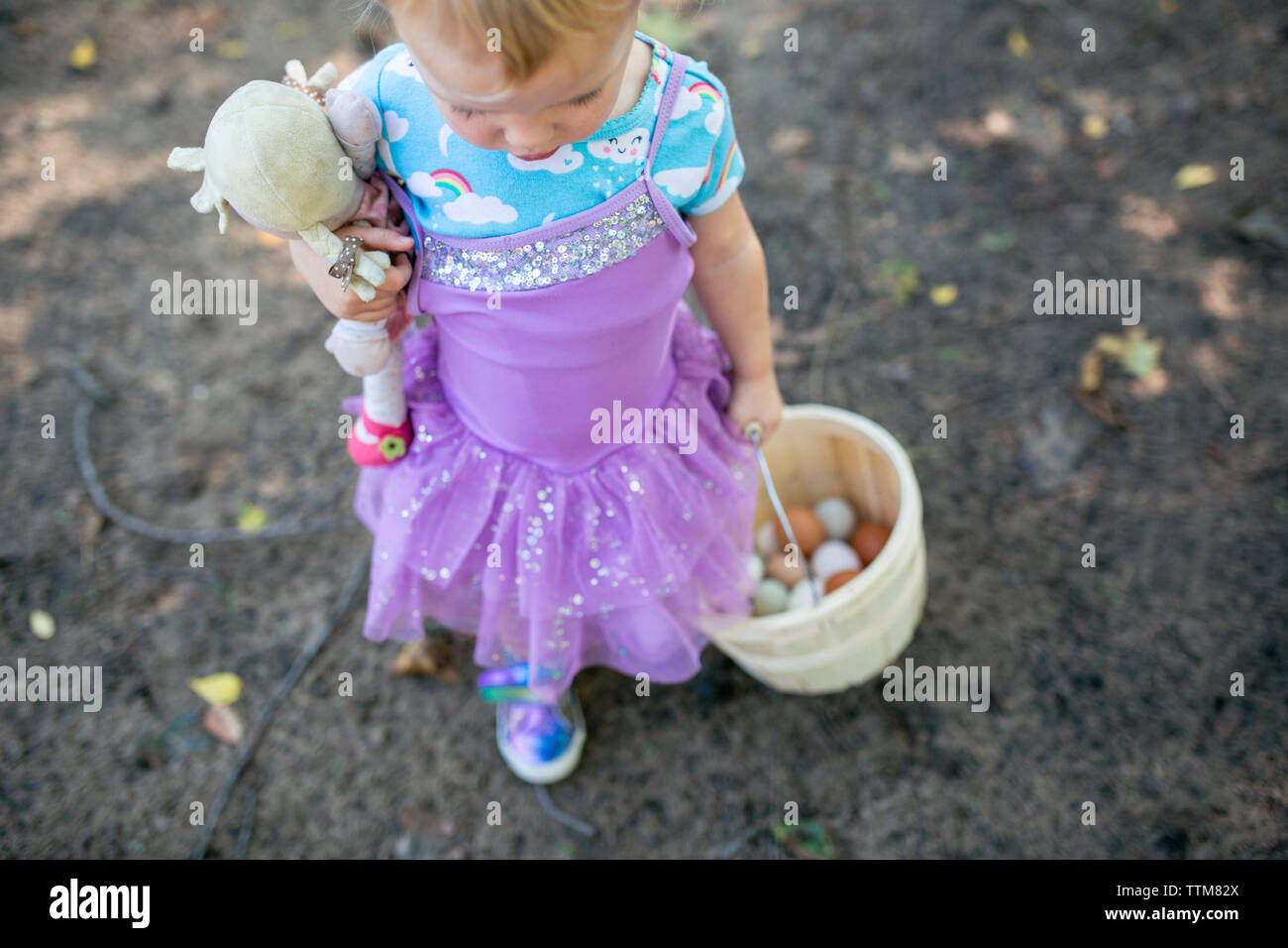 Toddler girl walking carrying basket of fresh eggs and baby doll Stock Photo