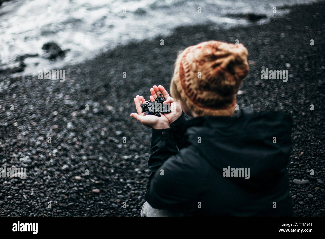 High angle view of woman holding pebbles while crouching on shore at beach Stock Photo