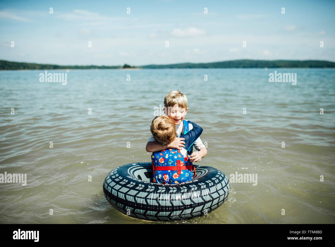 Brothers embracing in lake against sky Stock Photo