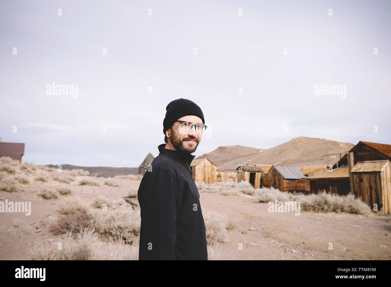 Portrait Of Man Standing By Log Cabins And Mountains Against Sky