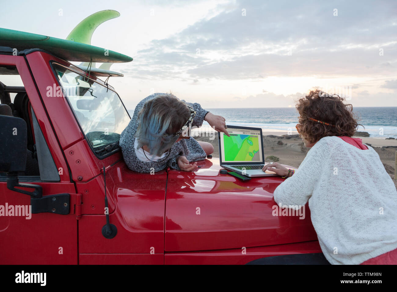 Two surfer girls  on their 4x4 car checking surf forecast on a laptop Stock Photo