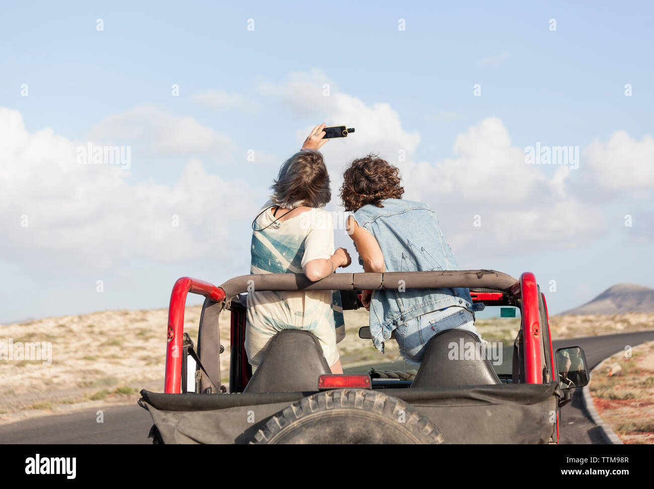 Two surfer girls  on a 4x4 jeep taking selfie Stock Photo