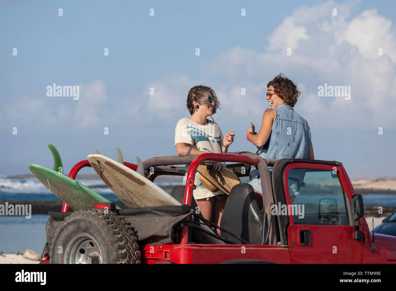 Two surfer girls standing one the seats of cabrio 4x4 car laughing Stock Photo