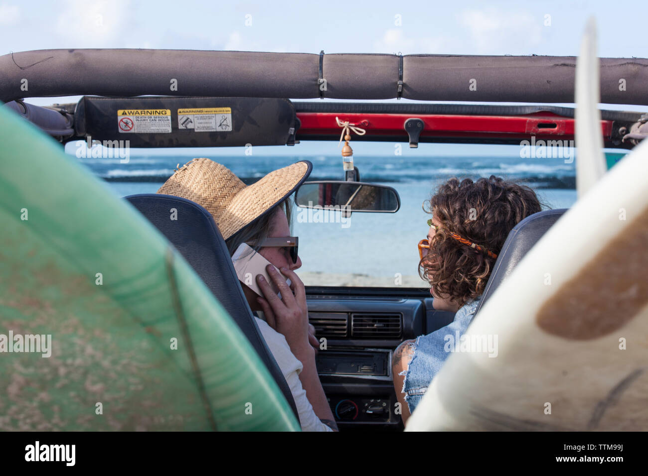 Two girls inside  cabrio 4x4 jeep with surfboards talking to the phone Stock Photo