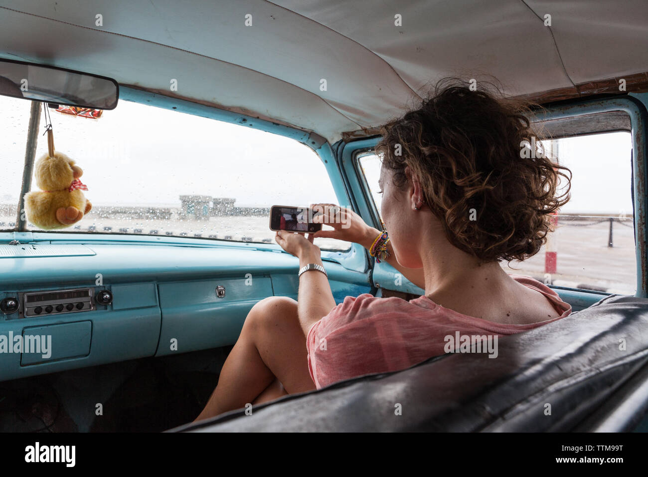 Western girl alone taking a selfie in an old vintage car in Cuba Stock Photo