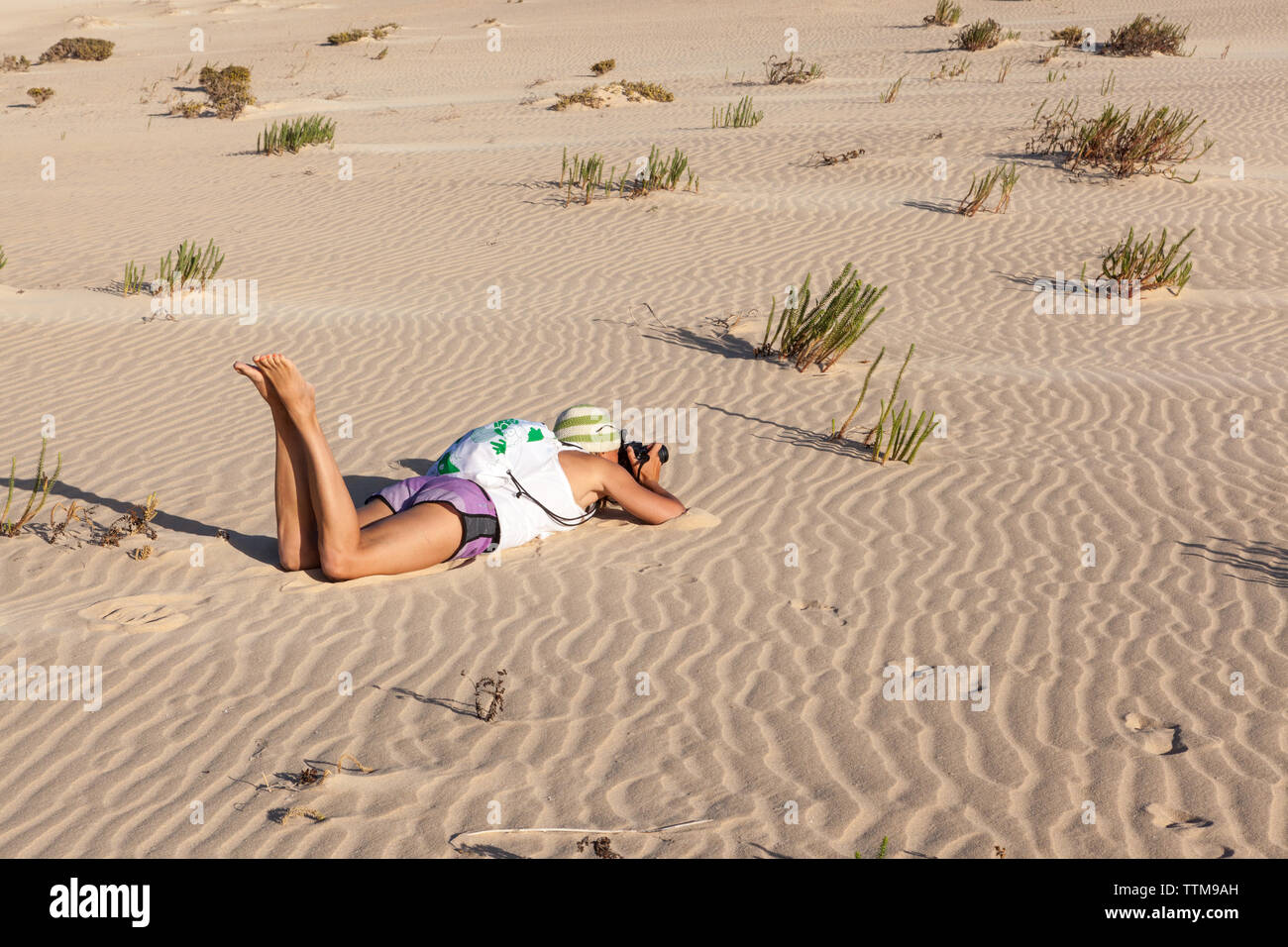 Girl in summer pants taking photo laying down in the sand Stock Photo