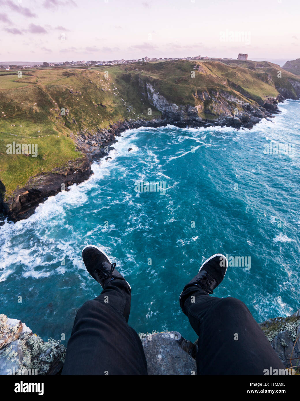 Low section of man sitting on cliff by sea against sky Stock Photo