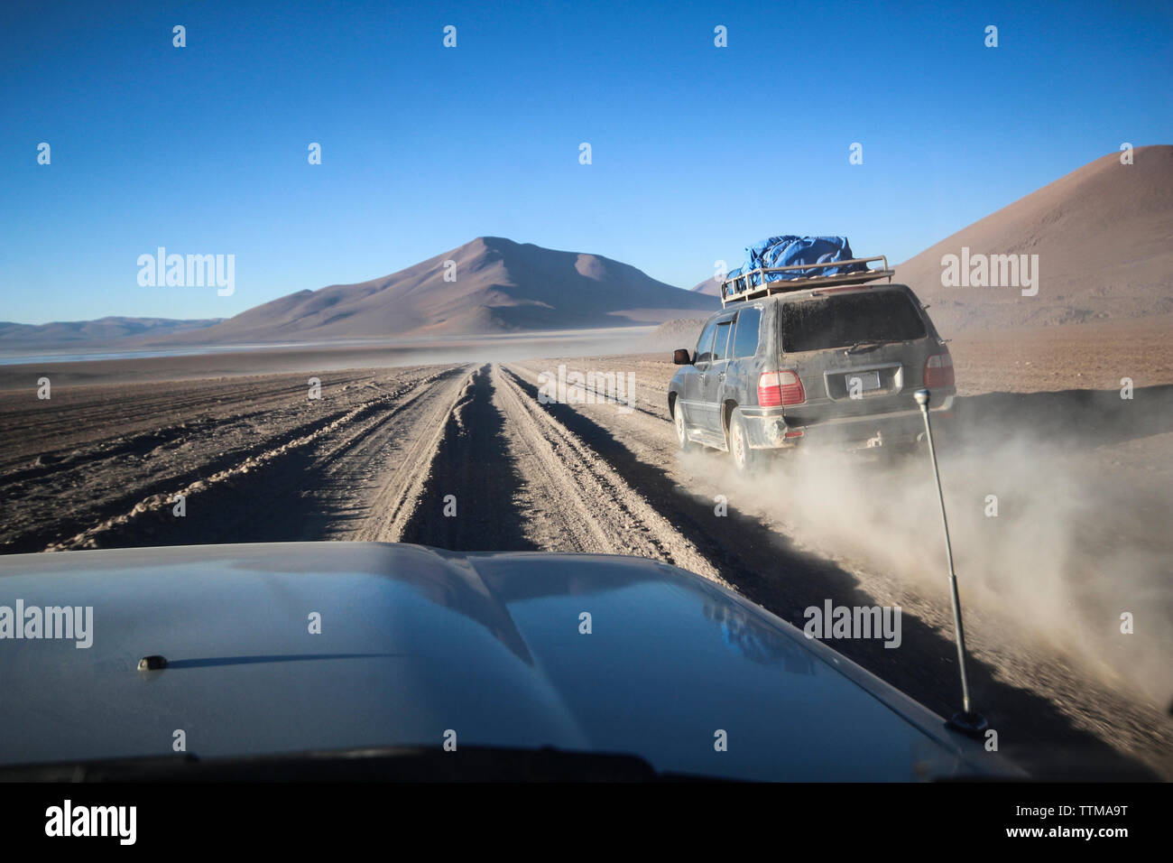 Off-road vehicles moving on dirt road against clear blue sky during sunny day Stock Photo
