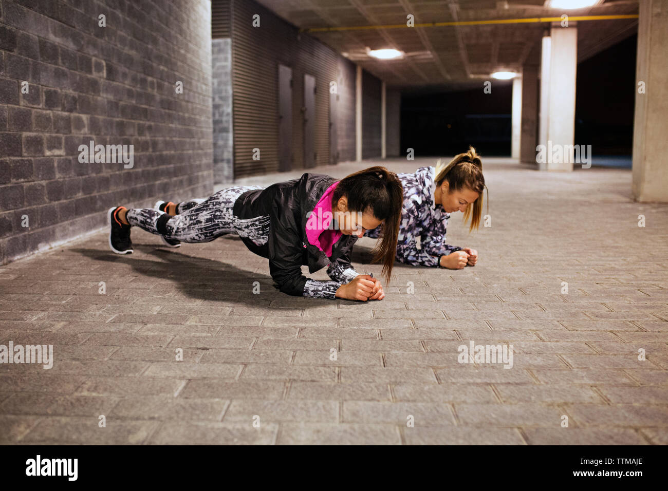 Determined female athletes doing plank exercises in tunnel Stock Photo