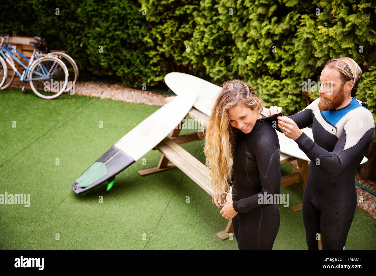 Man zipping up woman's wetsuit at lawn Stock Photo