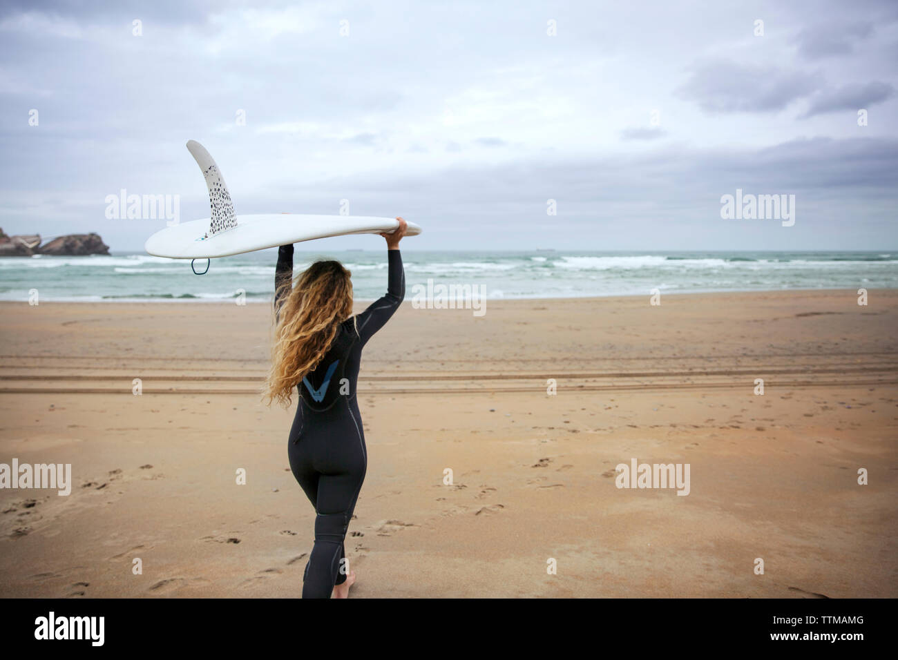Woman carrying surfboard while walking on beach against sky Stock Photo