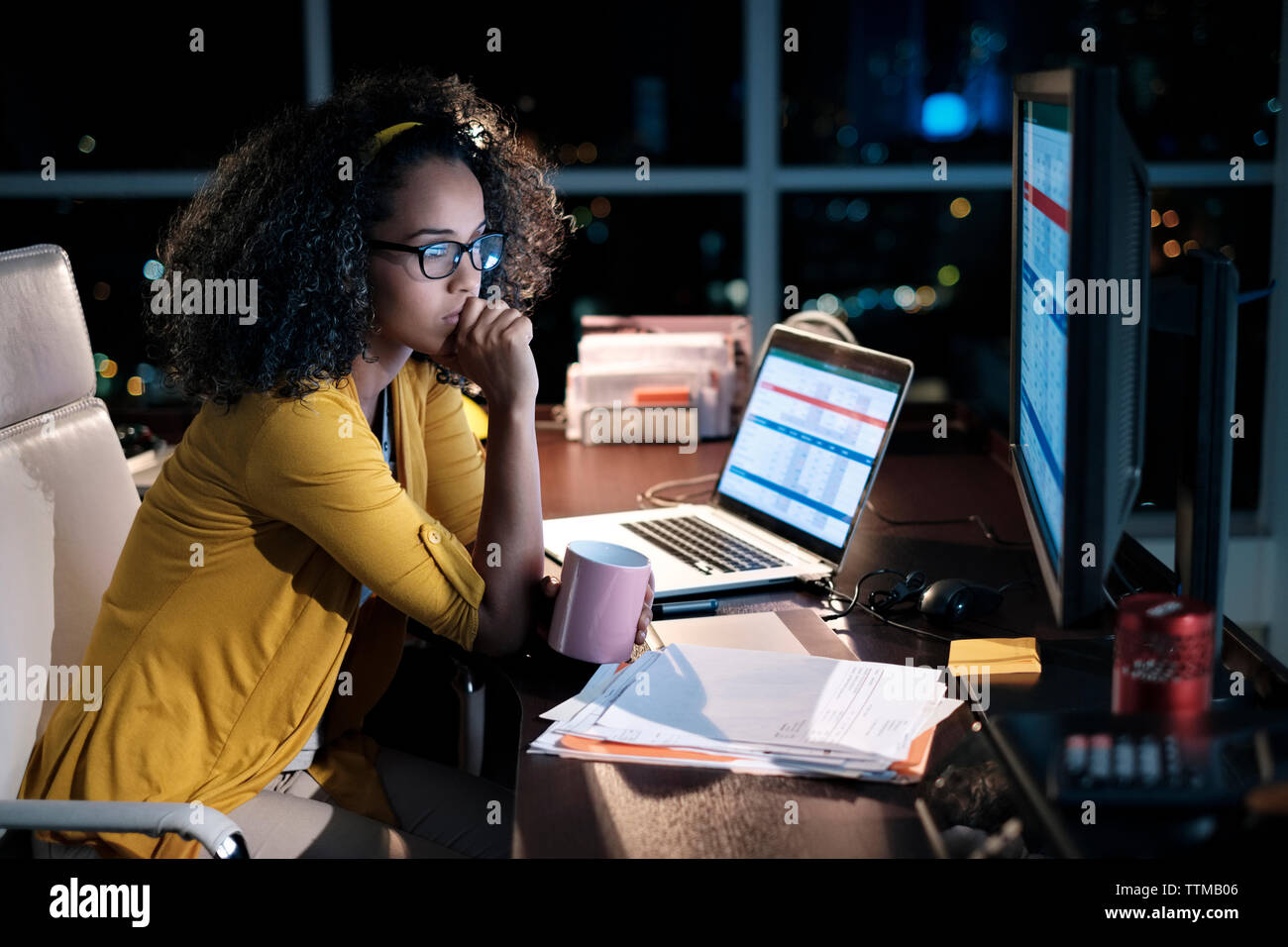 Thoughtful businesswoman holding coffee cup while sitting on chair in office at night Stock Photo