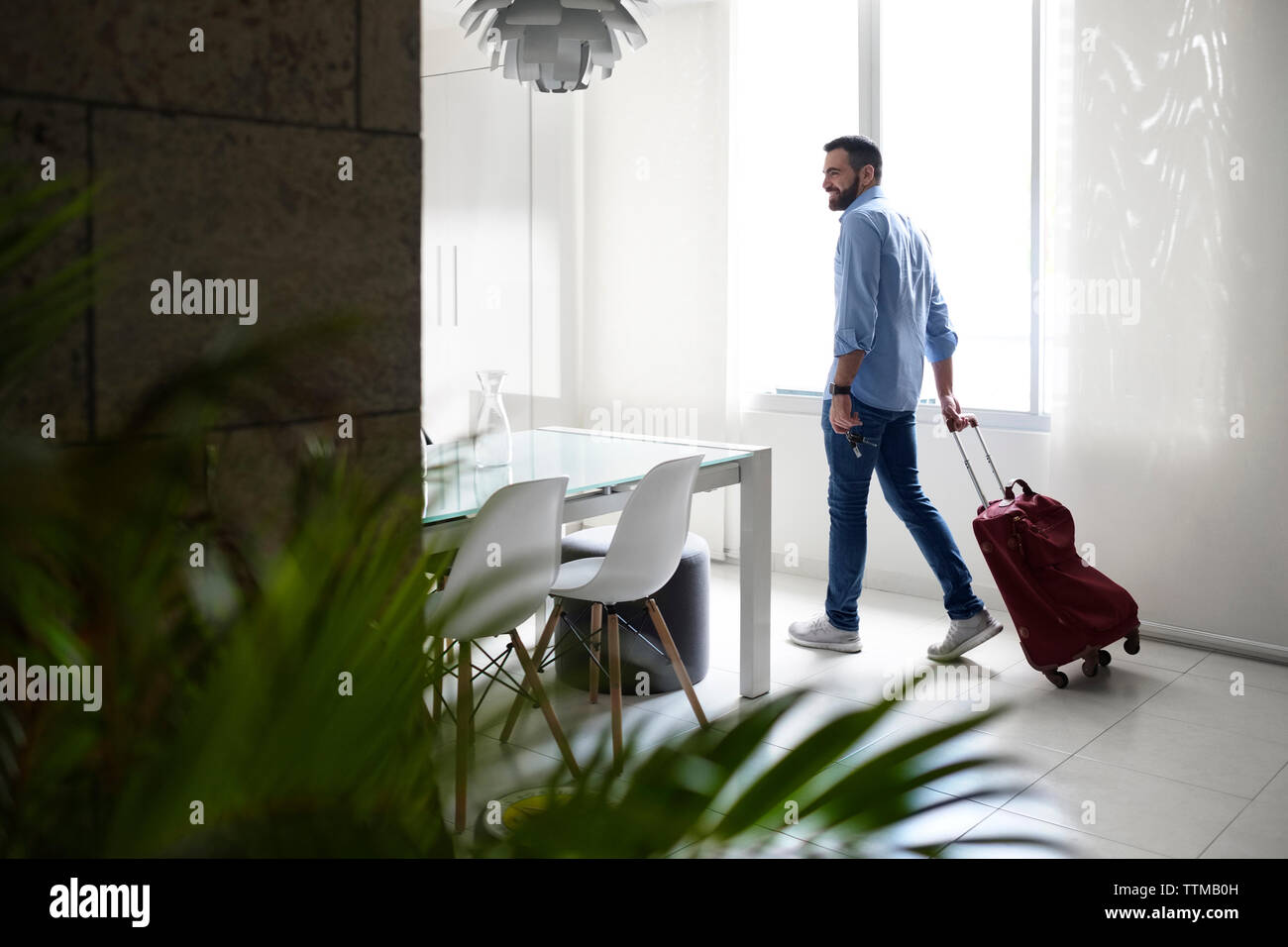 Full length of young man with luggage walking in rental house Stock Photo